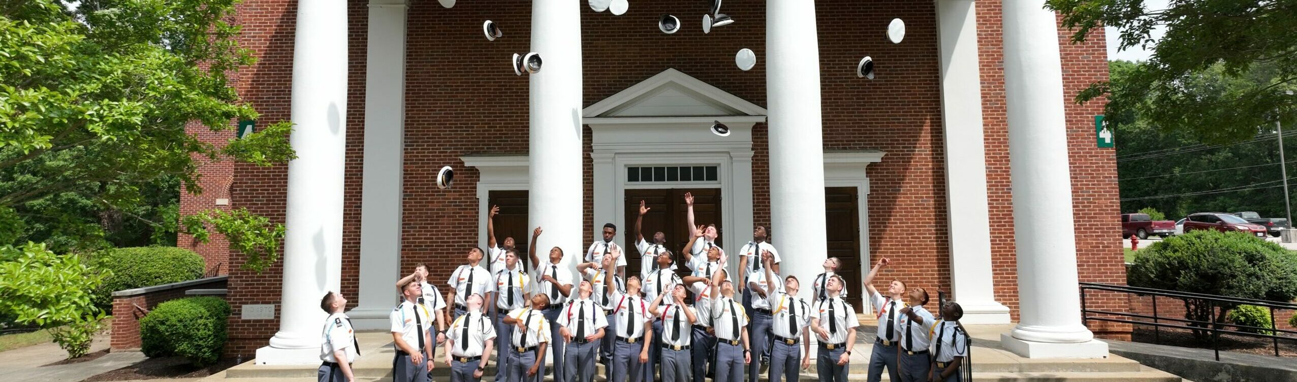 Senior cadets tossing hats in front of chapel.