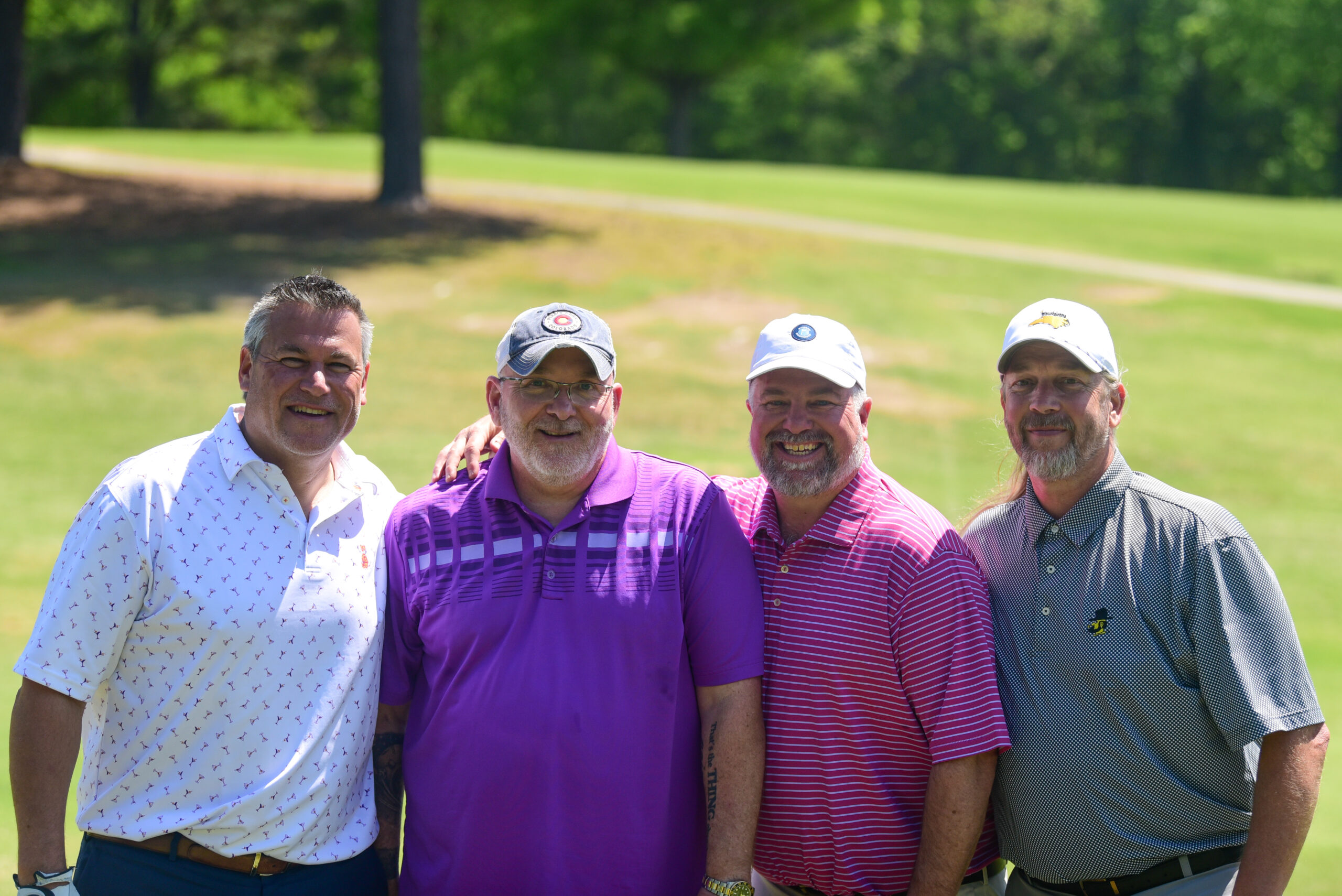 Four alumni smiling at the viewer during an alumni golf tournament.