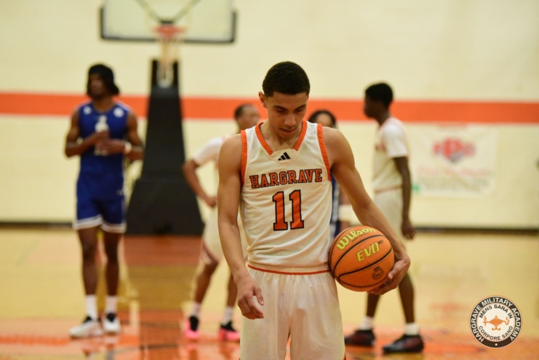 May show: A basketball player wearing a white Hargrave jersey with the number 11 holds a basketball on a court; other players and a hoop are visible in the background.